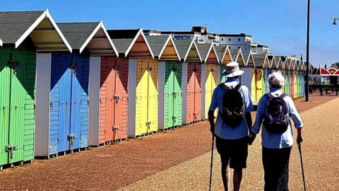 A couple walking along colourful huts on the beach