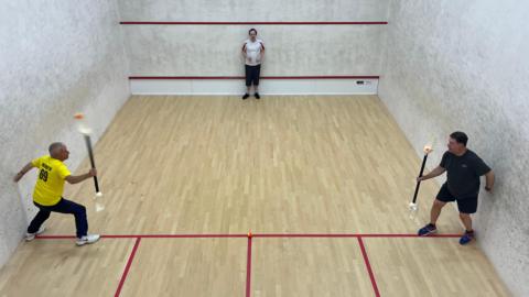 Three men on a squash court playing VX