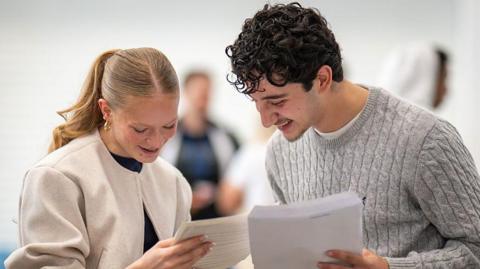 A girl and a boy open their results and look at their sheets of paper.