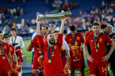 Spain defender Dani Carvajal raises the Uefa Nations League trophy aloft while wearing a gold medal. Team-mates Aymeric Laporte and Rodri are visible in the background.