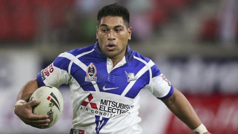 Matt Utai holds a rugby ball in his right hand and is wearing a blue and white shirt
