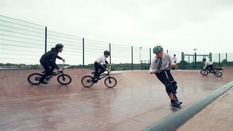 Four students ride their bikes and scooter on a purpose built skate park in their school yard.