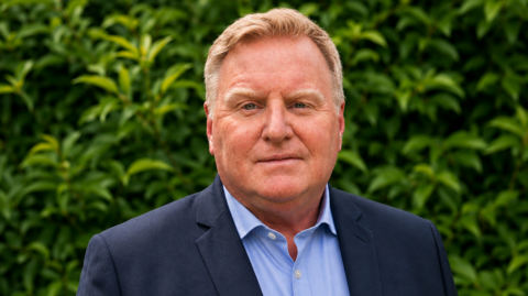 Andy Woolley has short blond hair. He wears a navy suit and a light blue shirt.