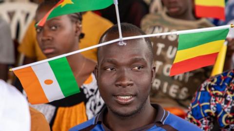 A supporter of the Alliance of Sahel States display the flags of Mali, Niger and Burkina Faso, during a rally in Bamako on 1 February 2024