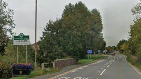 Street view of Tamworth Road, in Measham, Leicestershire, showing the Meashan village sign on the left.