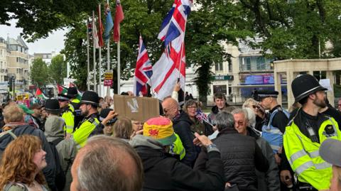 A group of people separated by police officers in hi-vis jackets. Some are holding Union Jack and St George's Cross flags.