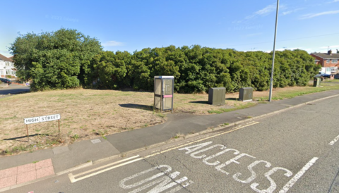 A Google street view image showing the High Street sign on a grassed area adjacent to a pavement running alongside the main road. Double yellow lines and an access only markings are on the road and there is a lamppost and trees in the background.