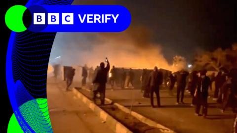 A group of protesters in Iran walking along a highway as smoke rises in the background
