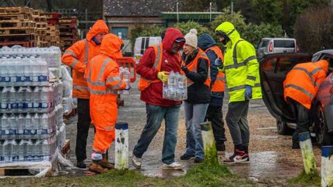 A group of people in high vis jackets picking up packs of bottled water.