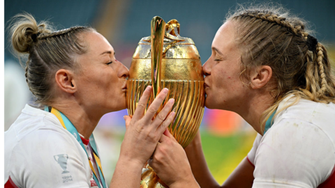 Natasha Hunt and Zoe Aldcroft kissing rugby world cup trophy.