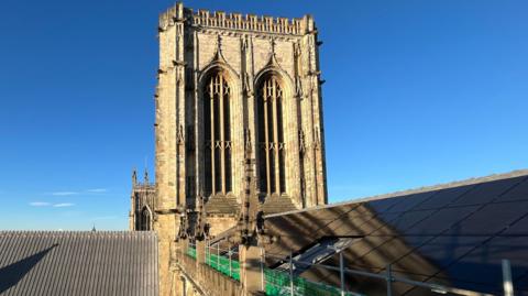 Solar panels on the roof of York Minster, with the sun shining against a blue sky.