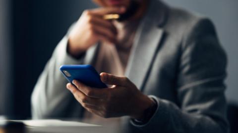 An anonymised man in a suit looks at a mobile phone