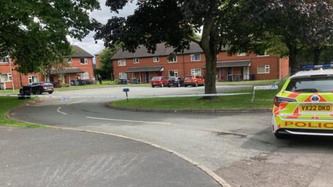 Street tapped off by blue and white police tape as a police car is parked at the entrance of the streey