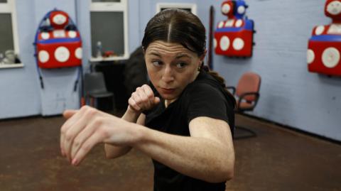 Emma Judd in a black T-shirt. She is shadow boxing close to the camera.