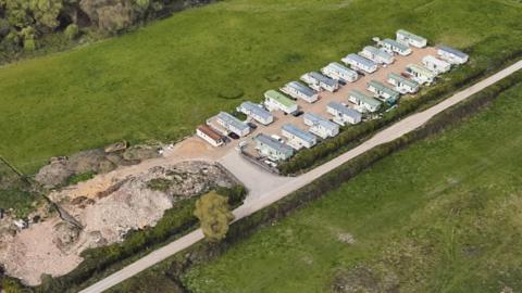 A bird's eye view of lines of caravans in field, next to a track