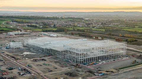 An aerial photo at sunset of the huge gigafactory steel frame on its construction site with the Somerset countryside surrounding it