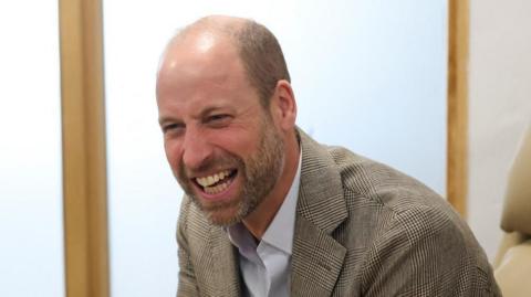 Britain's Prince William, The Duke of Cornwall, wearing a check jacket over an open neck shirt at the Isles of Scilly Hospital 