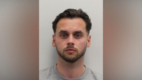 A custody image of a man with dark hair and a close cropped beard looking at the camera. 