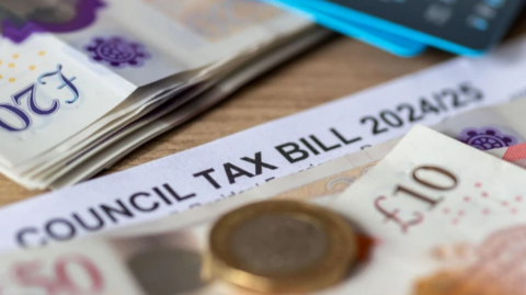 A council tax bill can be seen on a table with money on top. There are £10-notes and £20 notes and some coins.