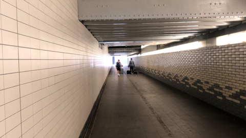 The underpass under the station, with two people walking ahead with suitcases