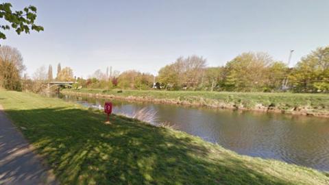 Generic image of the River Wye in Hereford, with grass on both sides of the river. There are several trees on the opposite side of the river to the camera and a bridge in the distance going across the river. 