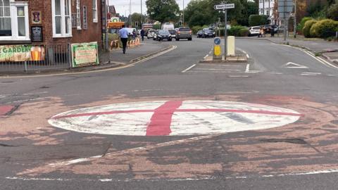 A mini roundabout which has been painted with the flag of St George - with a sign ahead of it that directs people towards Bromsgrove town centre.