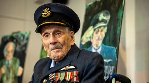 An RAF pilot in full uniform, navy jacket and hat with gold trim, and numerous colourful badges