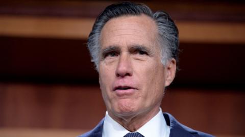 Utah Senator Mitt Romney, wearing a blue suit and shite shirt, pulls a facial expression