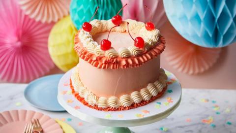 A heart shaped cake with pink icing with a background of hanging paper decorations