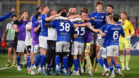 Como players, in blue shirts and socks and white shorts, celebrate in a huddle after securing Champions League qualification