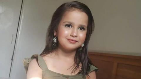 Sara Sharif smiling and looking at the camera. She has long, brown hair, long earrings and a green shirt on.