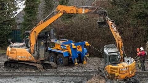 A digger being lifted out of mud