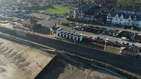 A drone image showing golden sands and a seafront dotted ith houses and huts.