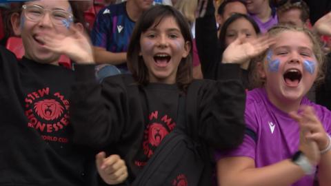 Three girls waving at the camera with scottish flags on their faces