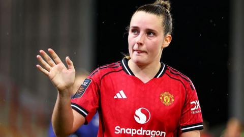 Ella Toone gives a signal with her right hand as she wears Manchester United's large red home shirt