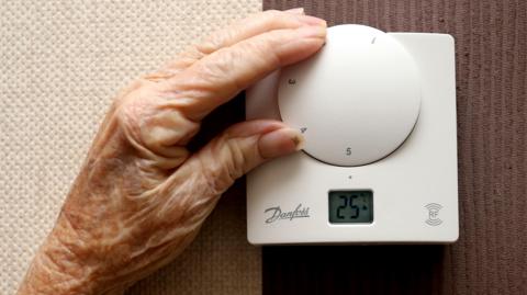 Elderly woman adjusts her thermostat
