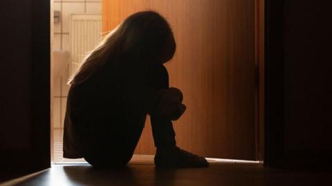A silhouette of a young girl sat on the floor outside a bathroom