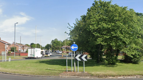 A sunny view of a roundabout with several trees growing in the middle of it.