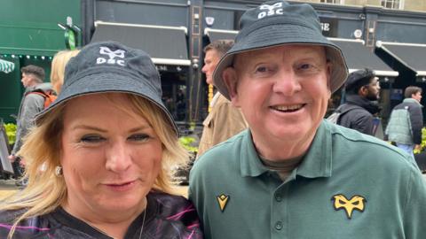 Annette Davies has blonde hair and is wearing a black Ospreys bucket hat. On the right Keith Collins is wearing a green polo shirt with an opsreys badge and a black Ospreys bucket hat. 