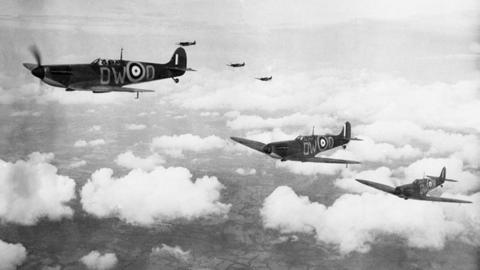 Three spitfires flying above the clouds. black and white image. It also shows three more spitfires in the background and fields can be seen below them