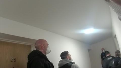 Police officers can be seen in a hallway, two of whom are wearing masks