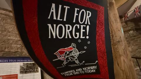 A giant banner with a man on skis with a Norwegian flag on his back and the heading Alt for Norge - All for Norway. Dumfries and Norway from 1940 to today is the sub-heading.