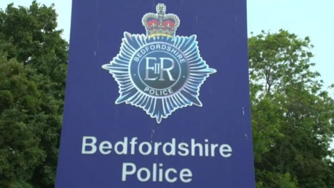 Sign saying Bedfordshire Police. The background it blue with the police crest above the wording.