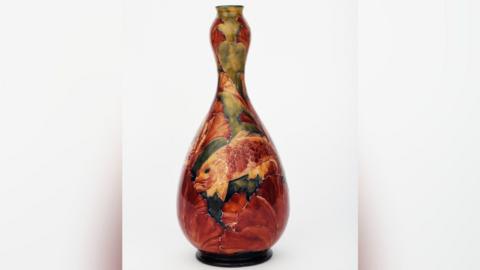 A tall, double gourd-shaped vase set against a white background. The vase has orange, green and red colours. The painted artwork shows fish swimming around the vase.