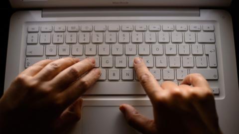 A picture of someone typing on a keyboard. It is a white keyboard.