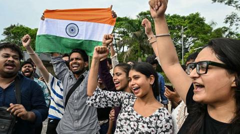 Five people celebrate, one holding an Indian flag