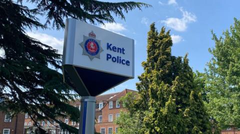 A sign reading KENT POLICE among some trees