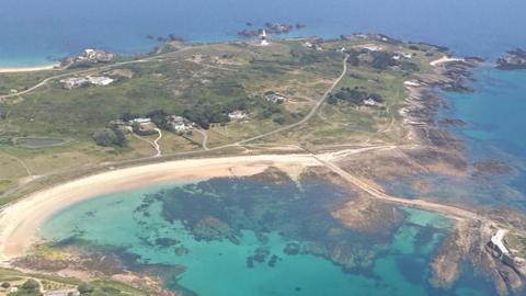 Aerial view of a coastal town with sandy beaches, rocky shoreline, turquoise bays, and patchwork fields stretching inland.