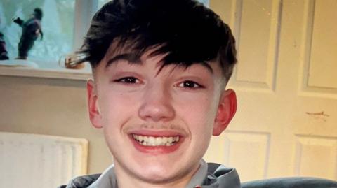 Christopher McBurnie, a teenager with short dark hair and a long fringe, smiling.