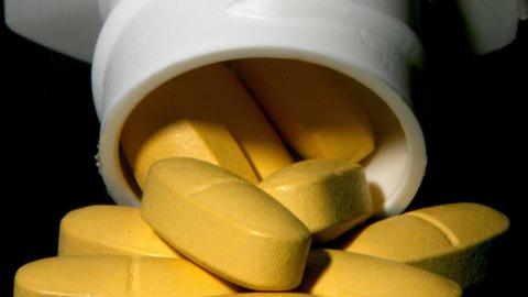 Yellow pills being poured out of a white medicine bottle.